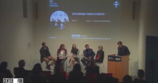 Video still from the event featuring panelists seated in discussion in front of a projector screen