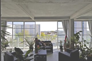 Photograph of an apartment in GRP Cite de Grand Parc showing a resident loungin on a couch with their dog in front of floor to ceiling windows