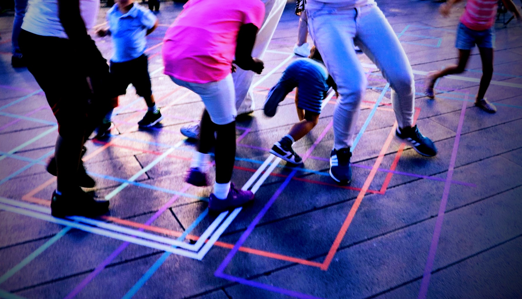 Adults and children dancing through taped lines on the ground