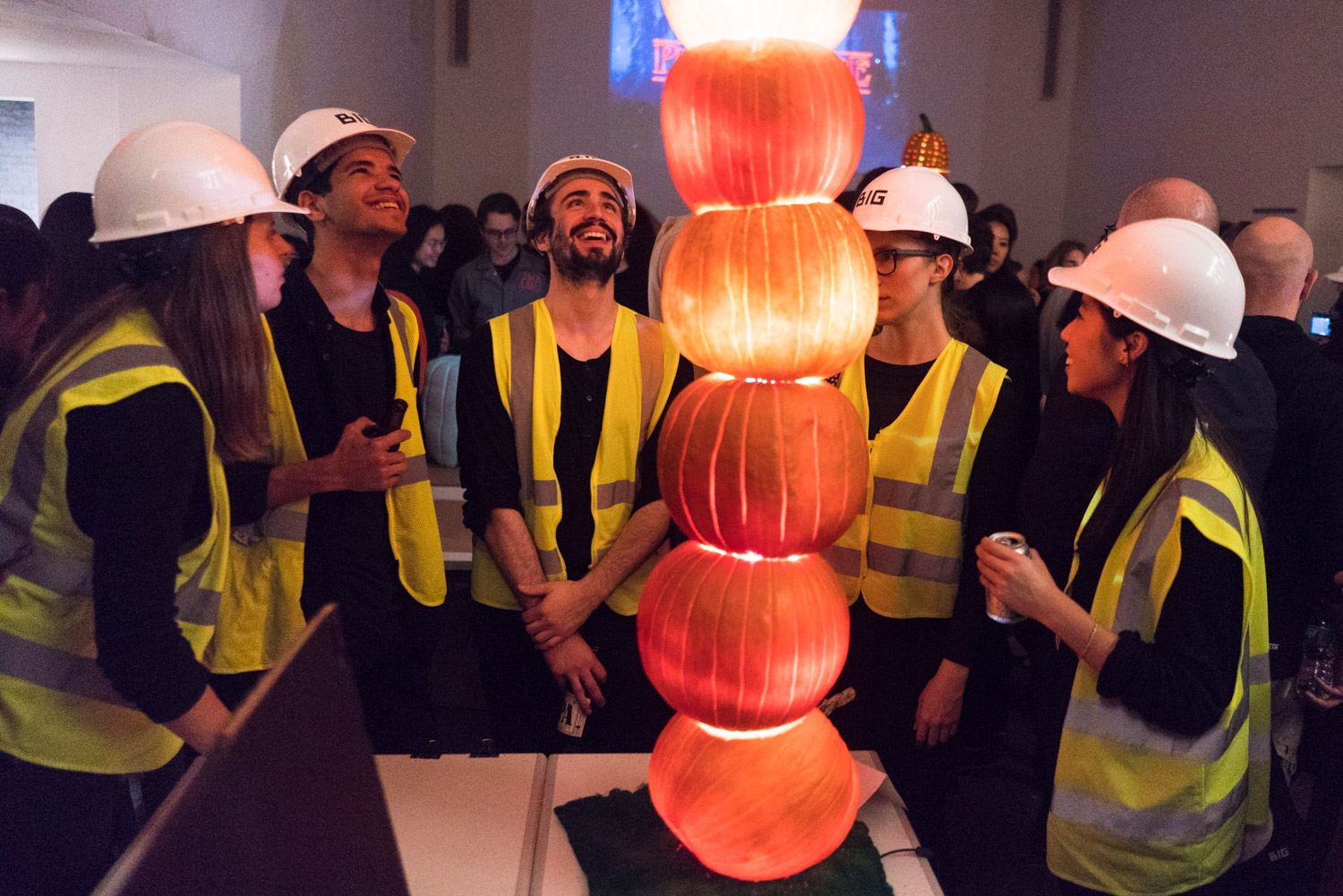 People in hard hats and vests surrounding a Pumpkitecture competition entry and looking at it