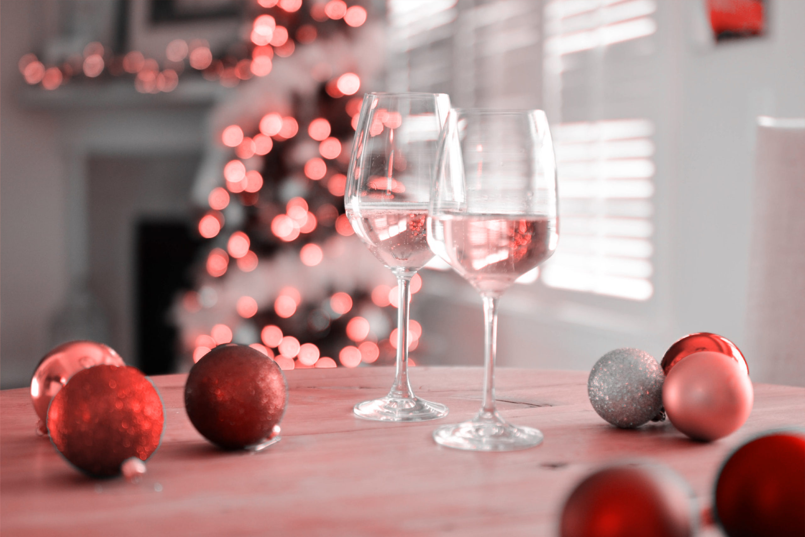 This is an image of two wine glasses on a tables surrounded by Christmas decorations.