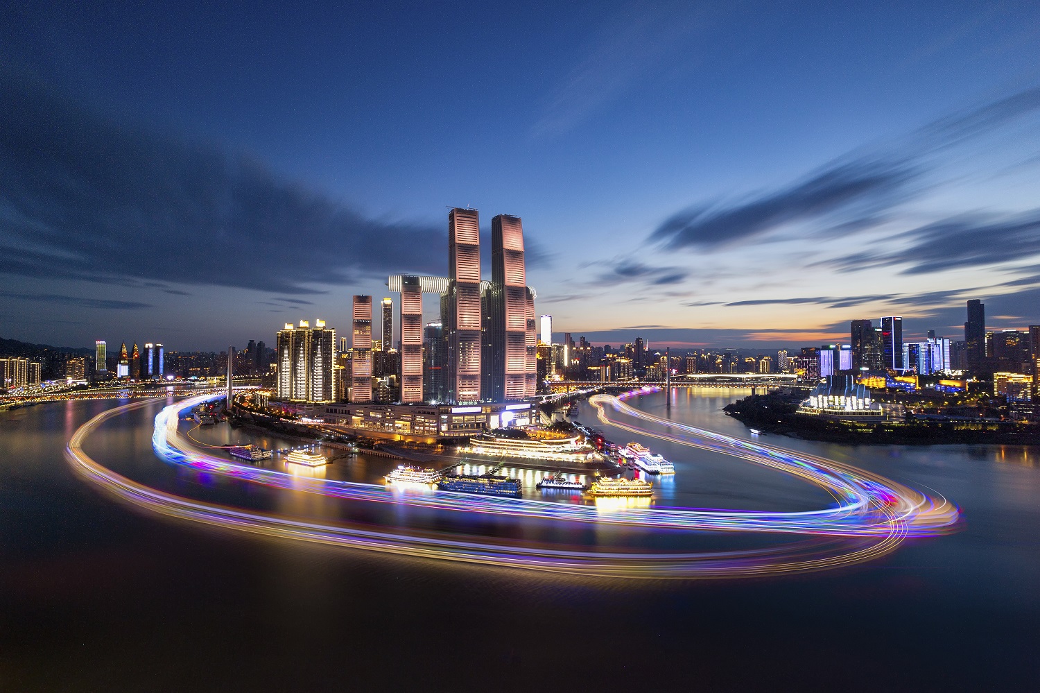 Long exposure photo of the Raffles City skyline. The photo is taken on a meandering river highlighting multiple highrise buildings lit up with multicolor lights