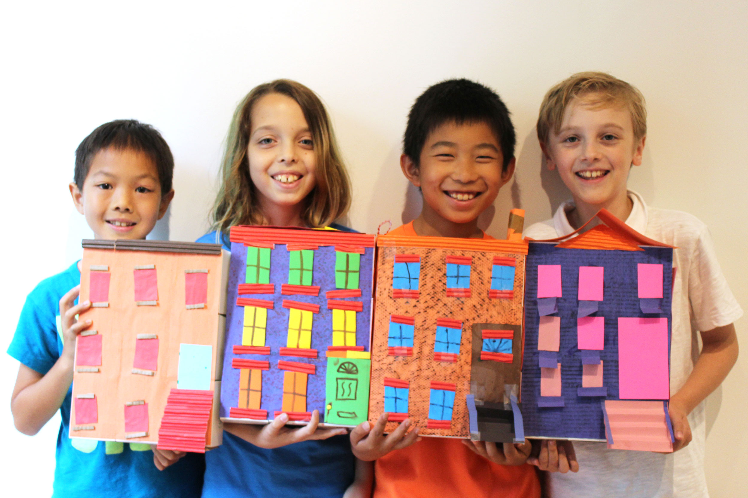 Four elementary school students holding their models of colorful rowhouses