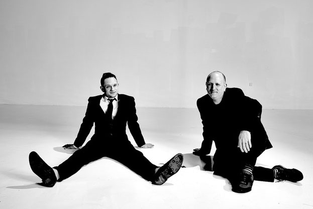 Black and white portrait of Evan Snyderman and Zesty Meyers seated on a white floor against a white background