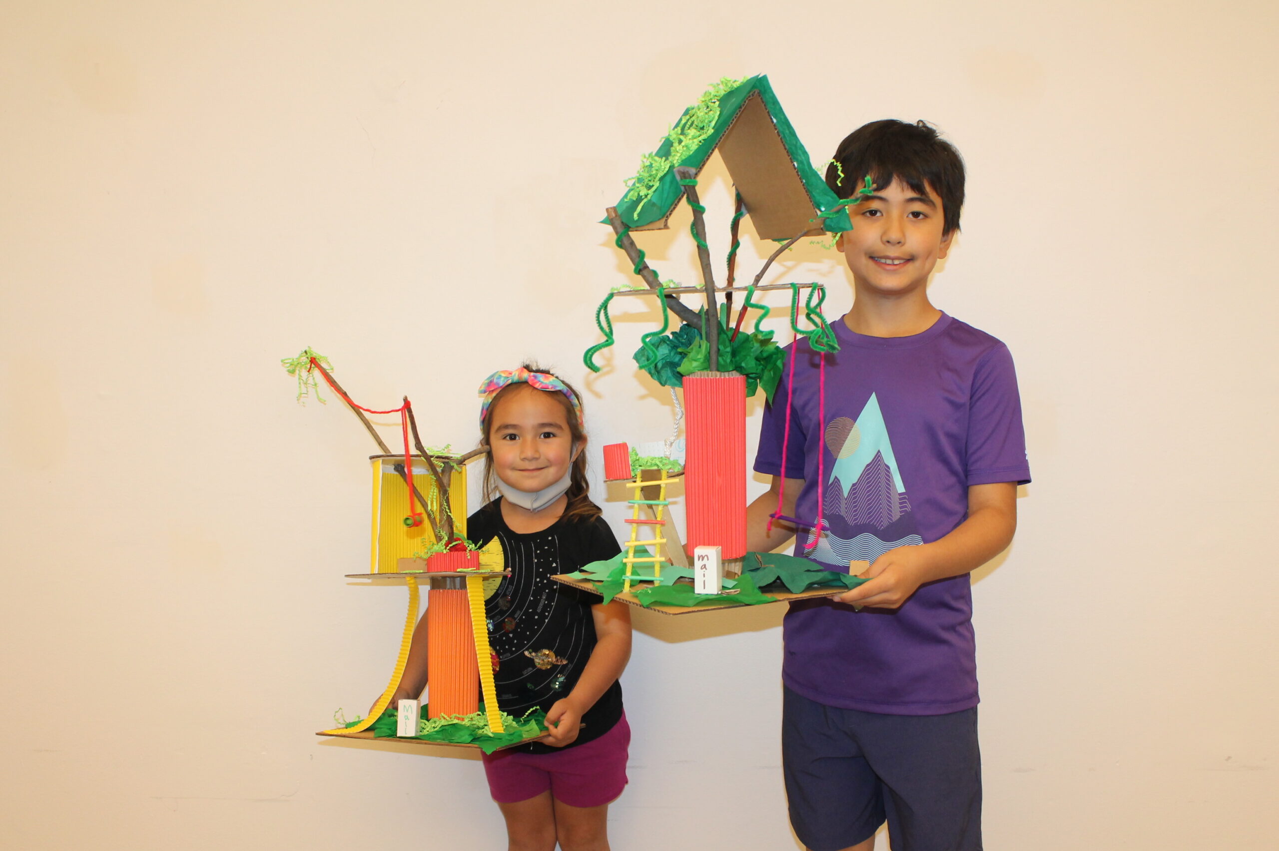 Two children holding model treehouses