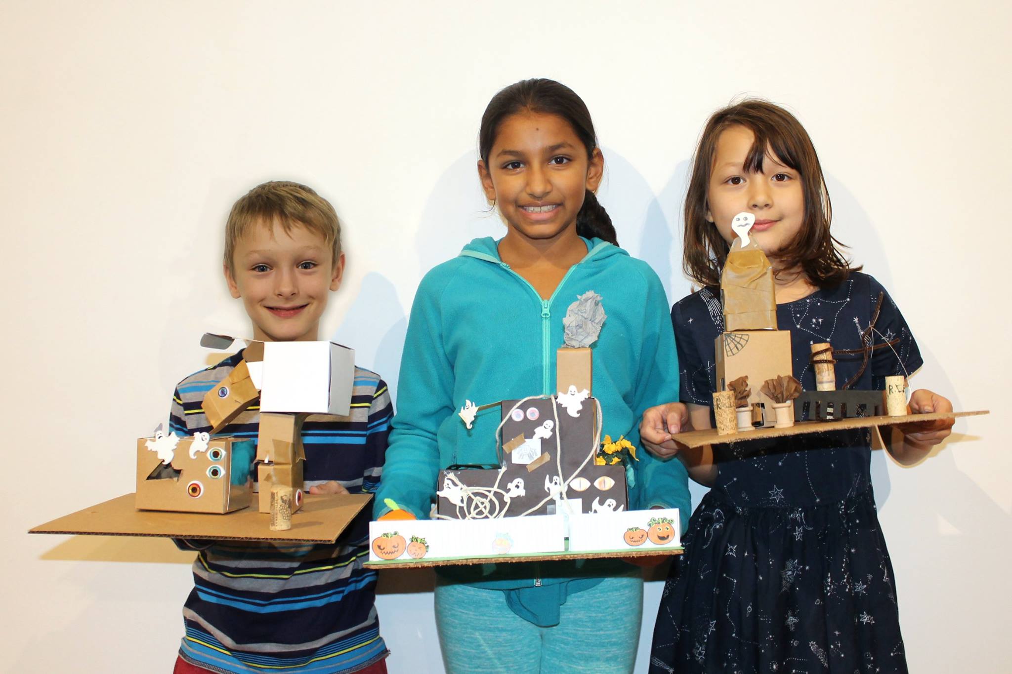 Three students holding models of haunted houses