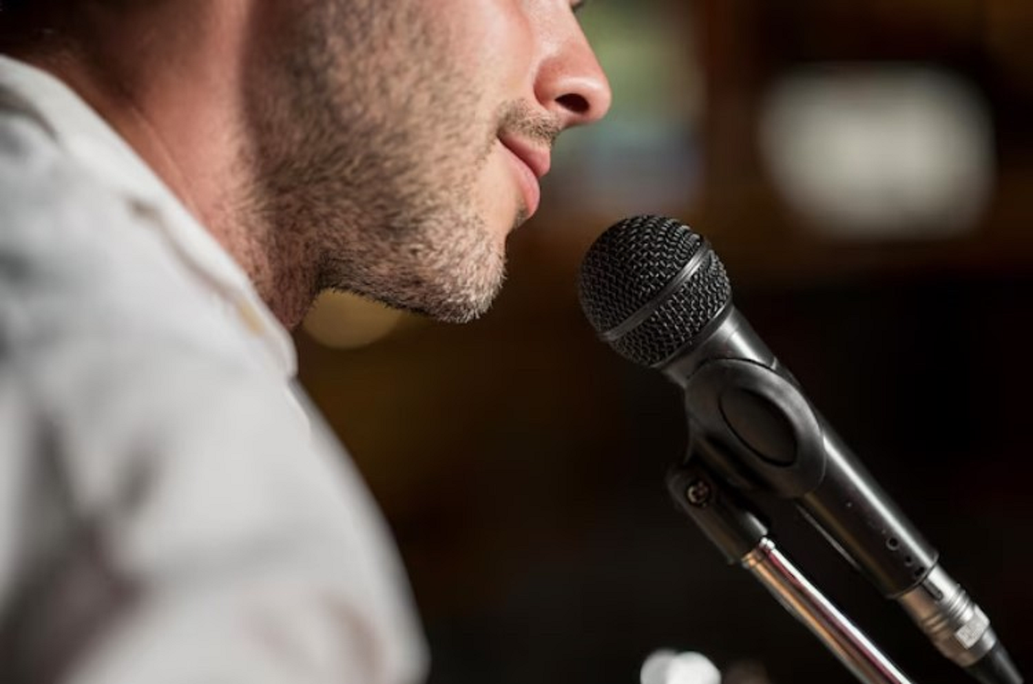 Closeup photo of a man speaking at a mic, zoomed in on the bottom half his face and the mic