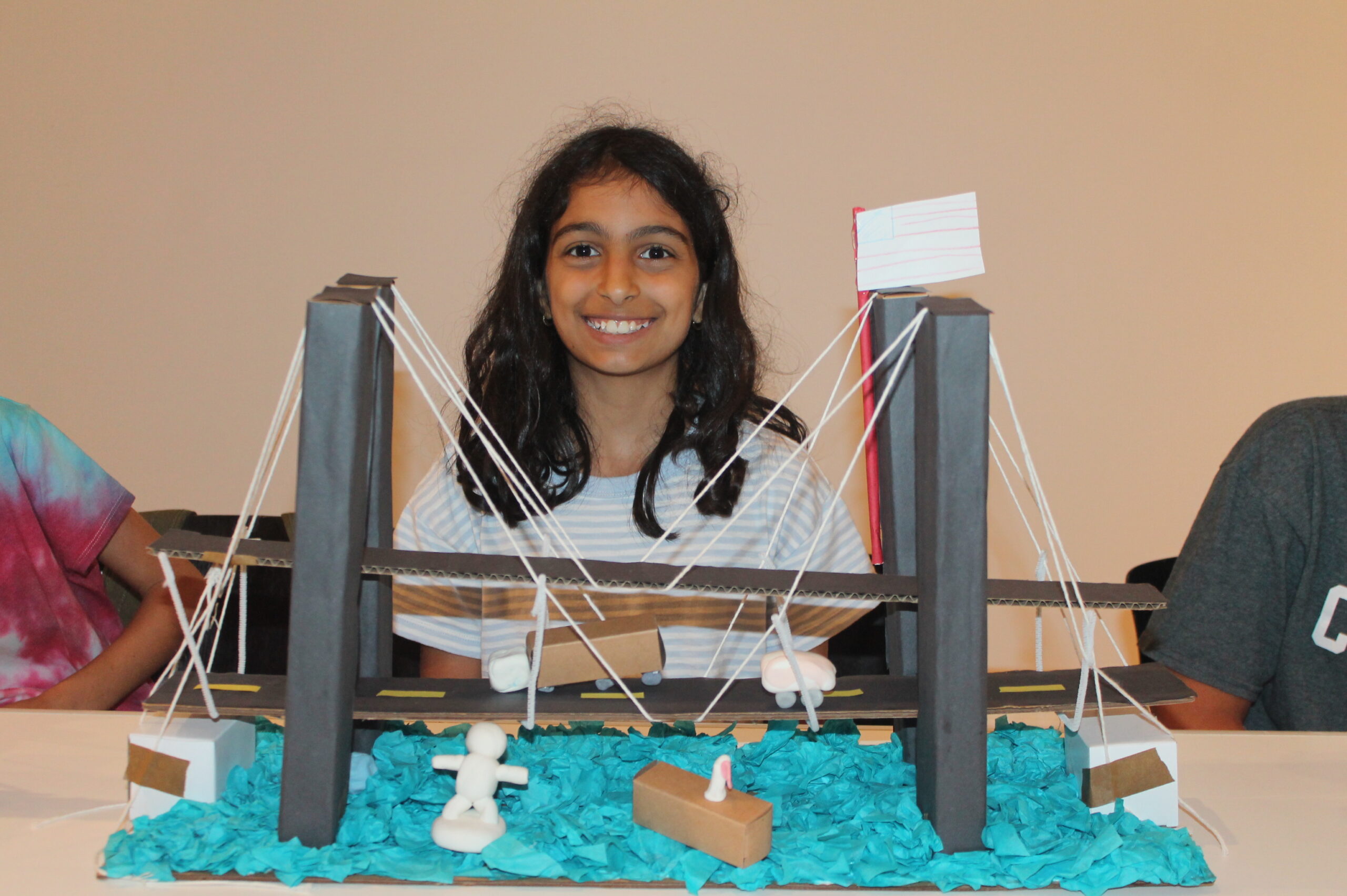 Elementary school student smiling behind her model of a suspension bridge