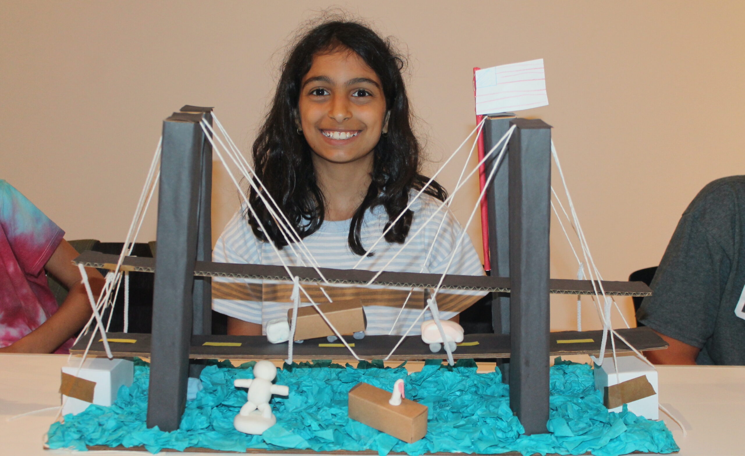 Elementary school student posing behind their model suspension bridge