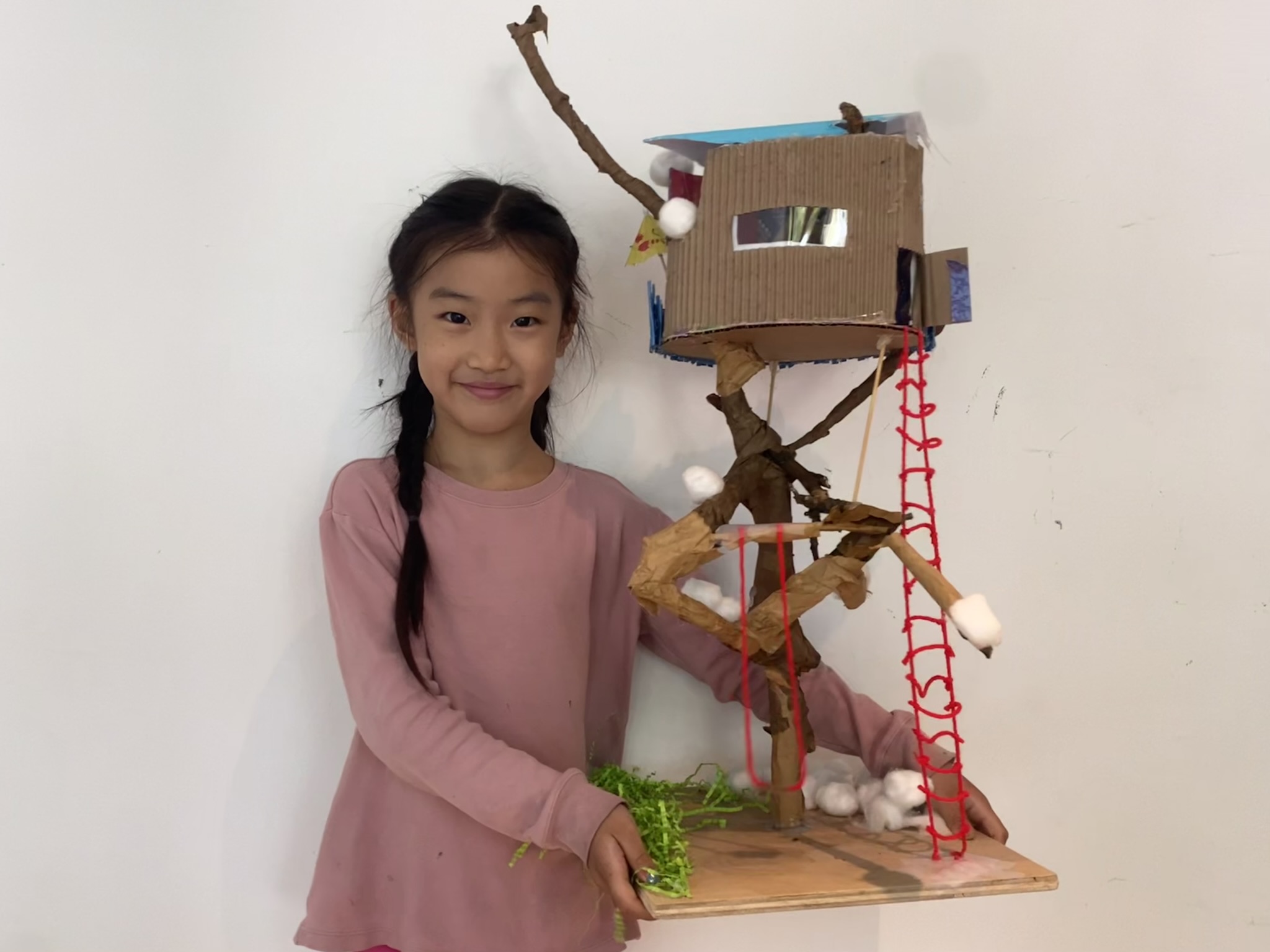 Elementary school student holding their model treehouse