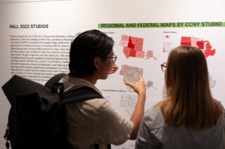 The backs of two people reading exhibition wall text and imagery.