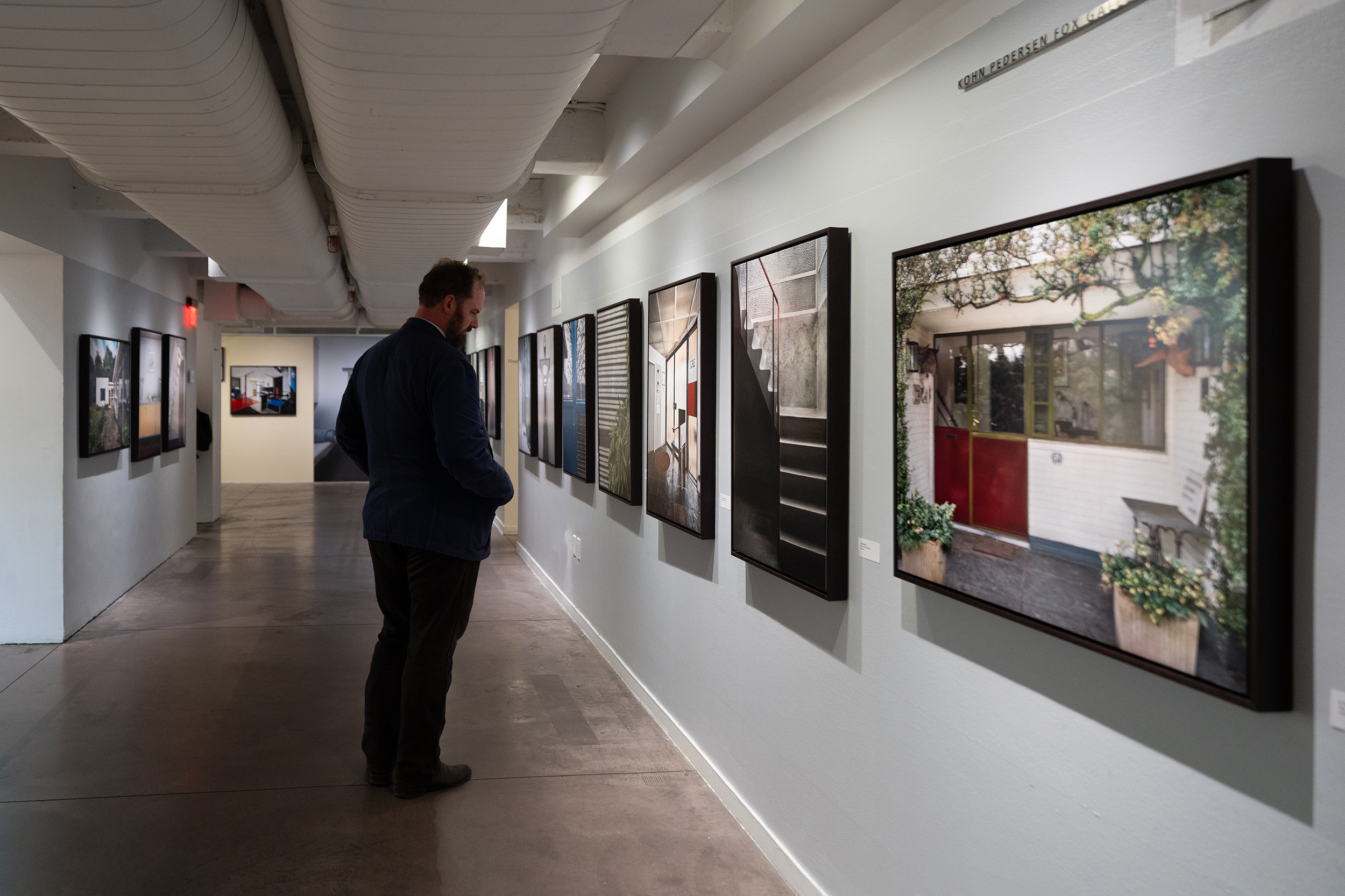 Man standing in front of a series of framed photographs in a long hallway