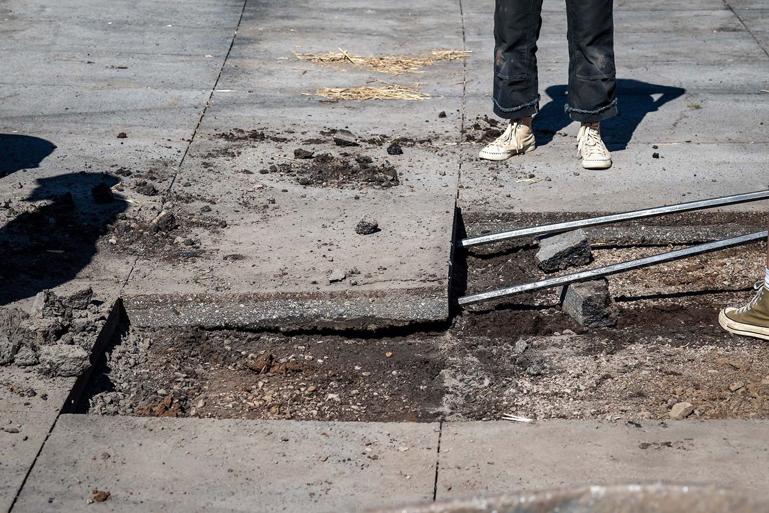 Sidewalk paver being lifted by metal fork with feet in the background