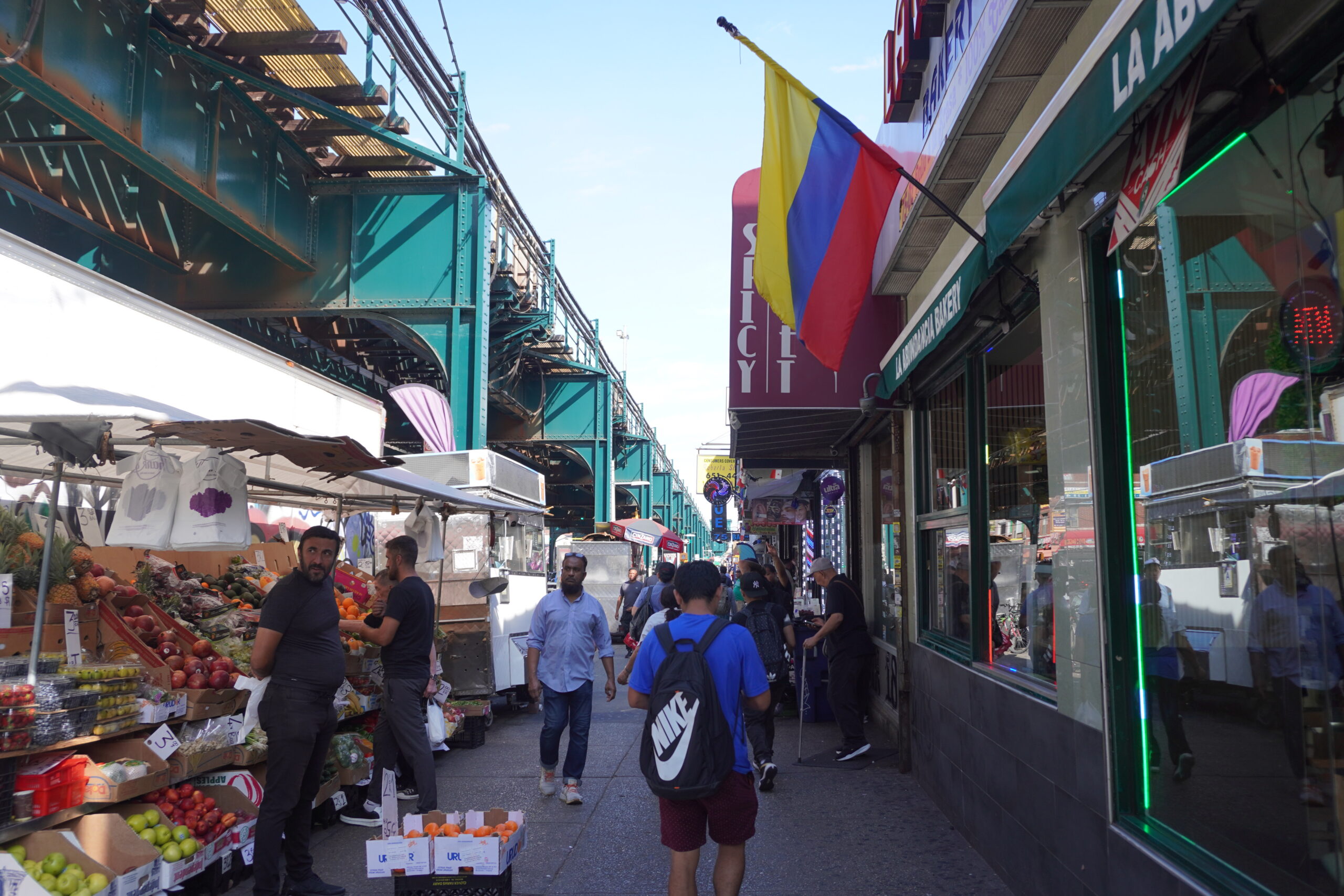 A streetscape underneath an expressway overhead with food stalls and pedestrians walking by